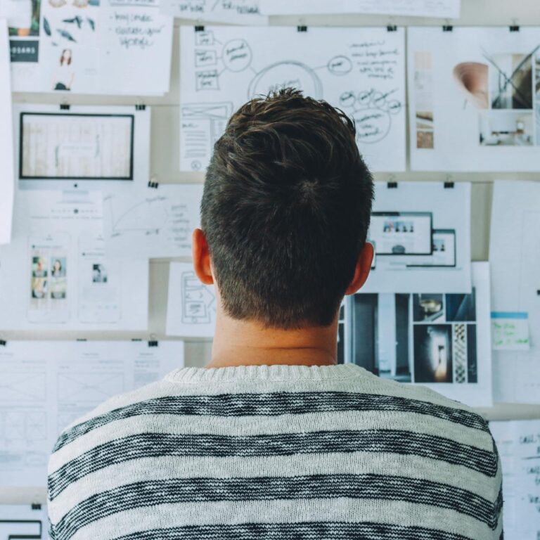 Man Wearing Black and White Stripe Shirt Looking at White Printer Papers on the Wall